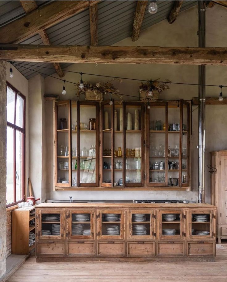 an old fashioned kitchen with wooden cabinets and dishes on the counter top in front of large windows