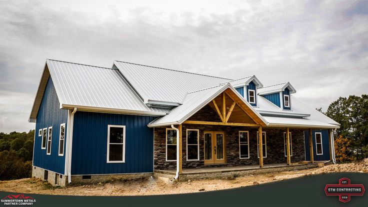 a blue and white house sitting on top of a dirt hill with trees in the background