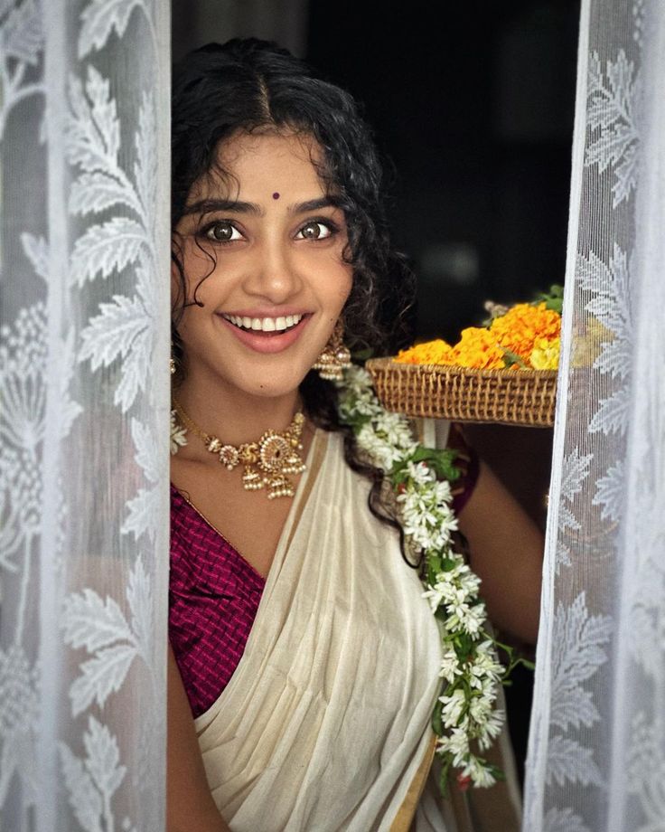 a woman wearing a white sari with flowers in her hair and smiling at the camera