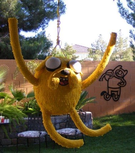 a yellow stuffed animal hanging from a chain in the yard with its arms and legs stretched out