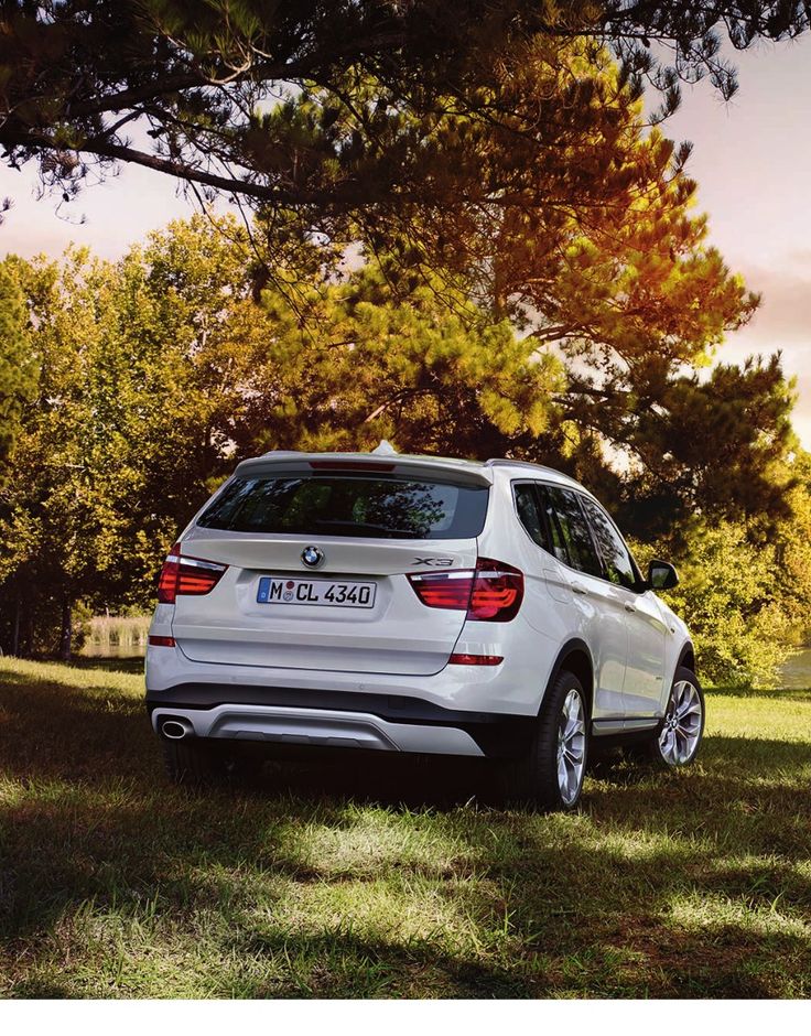 the rear end of a white bmw suv parked on grass in front of some trees