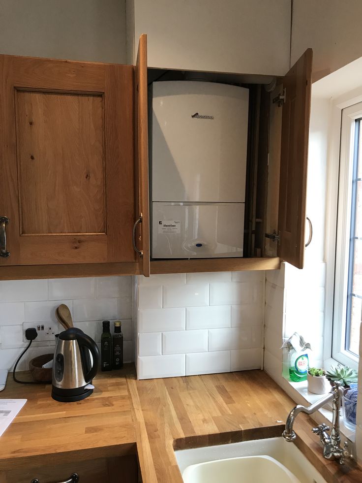 a kitchen with wooden cabinets and white tile backsplash, sink and tea kettle