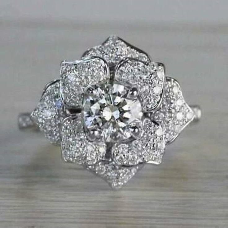 a white gold diamond flower ring on a wooden table with the center stone surrounded by smaller diamonds