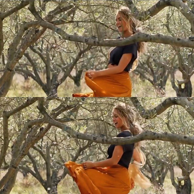 the woman is wearing an orange skirt while standing on a tree branch with her hands in her pockets