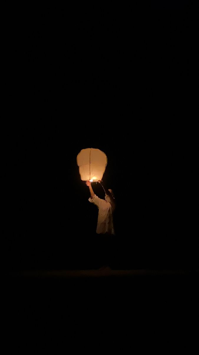 a person holding a paper lantern in the dark with one light on their hand and another flying through the air