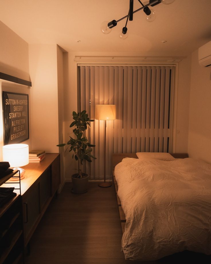 a bed sitting in a bedroom next to a lamp on a wooden dresser under a window