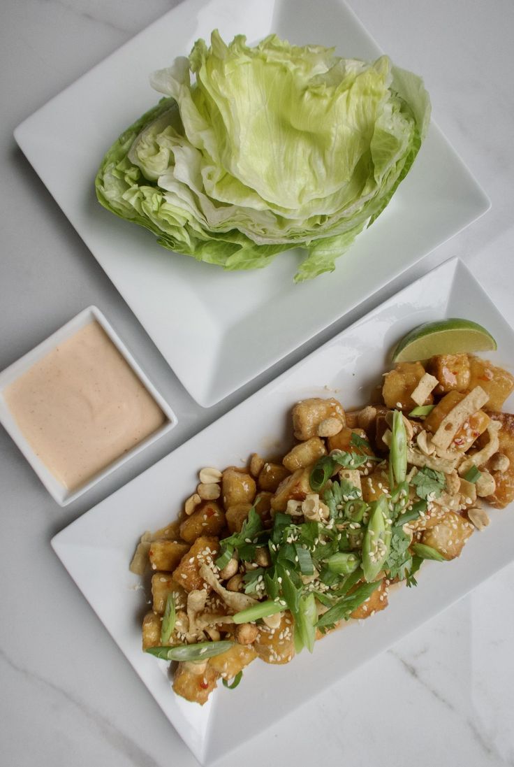 two white plates topped with lettuce and chicken next to a bowl of sauce