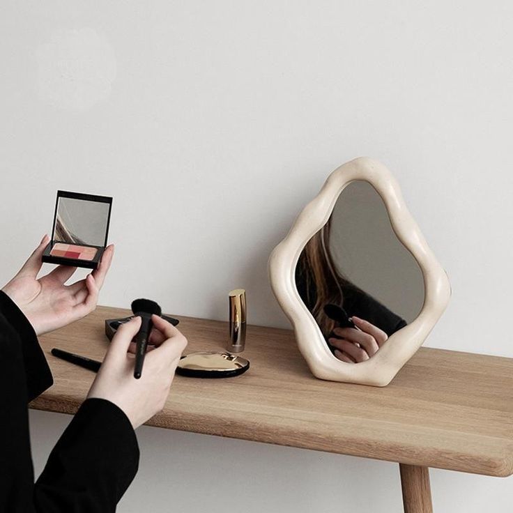 a woman holding a small mirror next to a wooden table