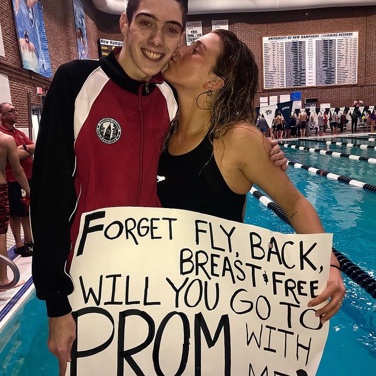 two people standing next to each other in front of a swimming pool holding a sign that says forget fly back, breast free, will you go to prom with me