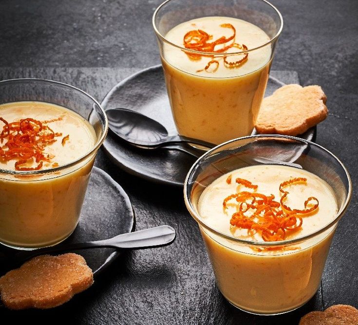 three desserts with orange garnishes and cookies on black plates next to each other