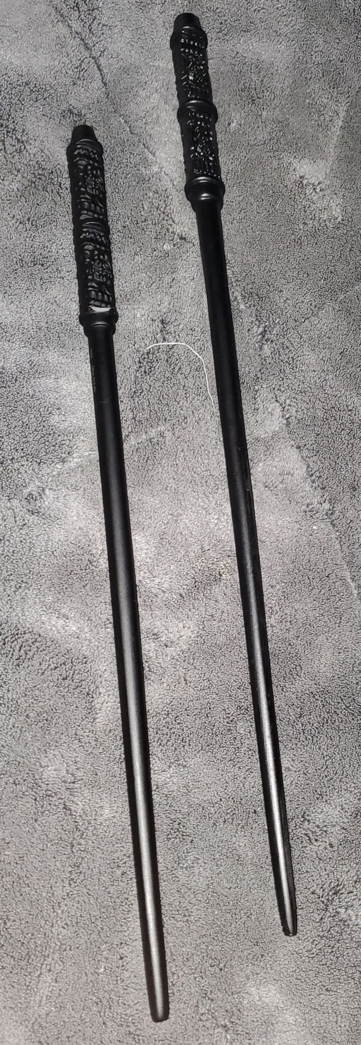 two black swords laying on top of a gray carpet next to each other and one has a pointed tip