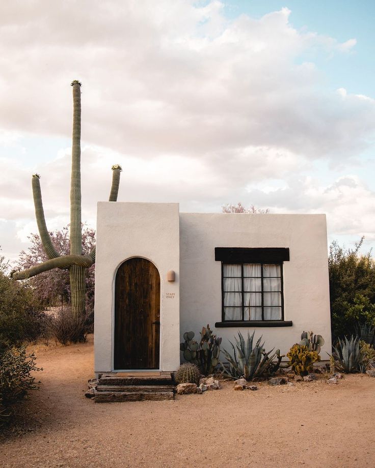 an adobe style house with cactus and cacti in the foreground on a cloudy day