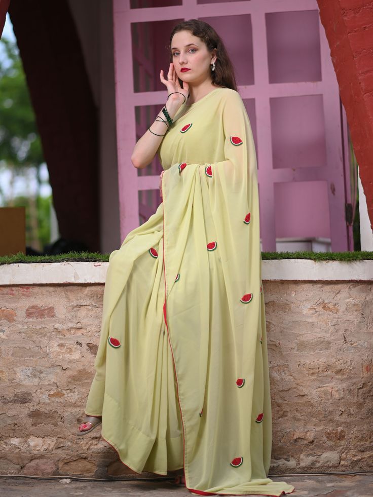 This is a three-piece watermelon saree set from the Ensembles collection. The pistachio green saree is paired with a matching sleeveless blouse. There are beautiful watermelon motifs of red, green, and white bead work all over the saree. This saree set is crafted in faux georgette fabric with contrast piping border. The outfit is completed with a heavily embellished, beadwork red, green and white watermelon shape handbag. Green Sleeveless Pre-draped Saree For Festive Season, Designer Wear Summer Sharara With Traditional Drape, Pista Green Georgette Pre-draped Saree With Dupatta, Summer Traditional Georgette Pre-draped Saree, Summer Traditional Drape Pre-draped Georgette Saree, Summer Sharara With Zari Work, Summer Sharara With Zari Work And Traditional Drape, Summer Traditional Drape Sharara With Zari Work, Traditional Drape Sharara With Zari Work For Summer