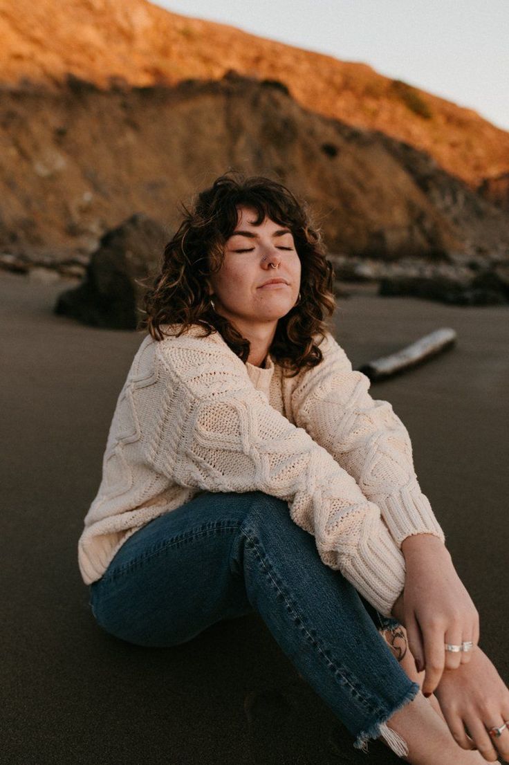 a woman is sitting on the beach with her eyes closed and she is looking up