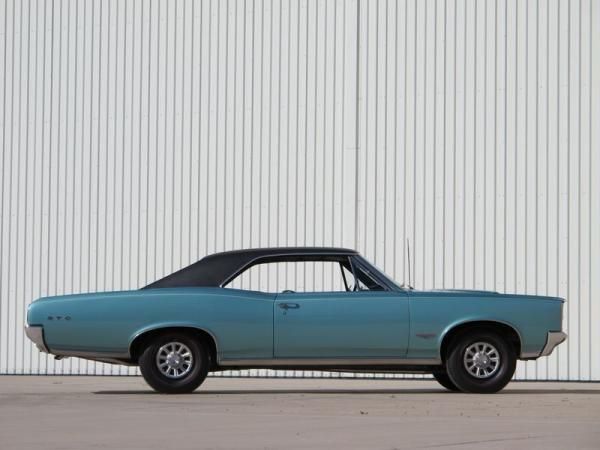 an old blue car parked in front of a white building with a metal wall behind it