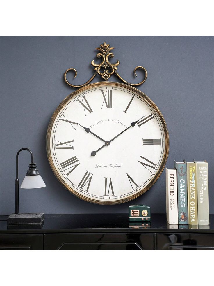 a large clock on the wall next to a lamp and some books in front of it