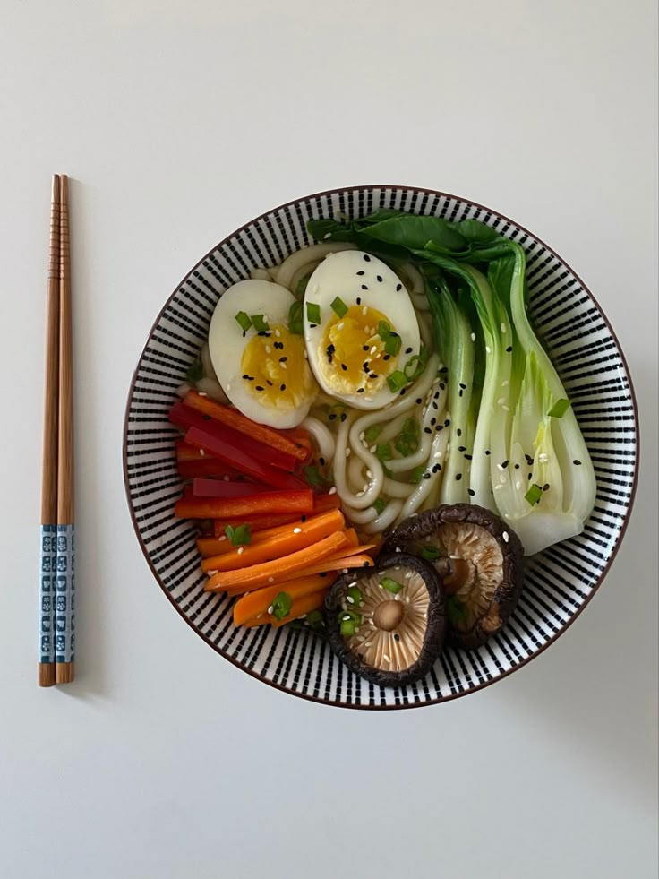 a plate with noodles, carrots, mushrooms and an egg on it next to chopsticks