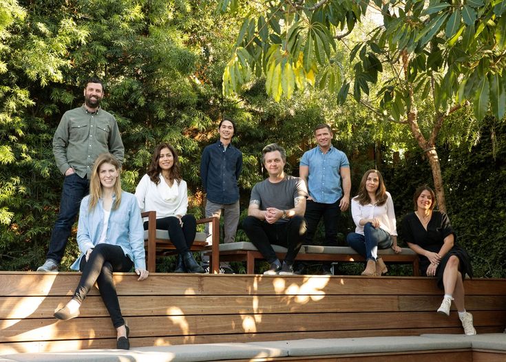 a group of people sitting on top of a wooden bench next to trees and bushes