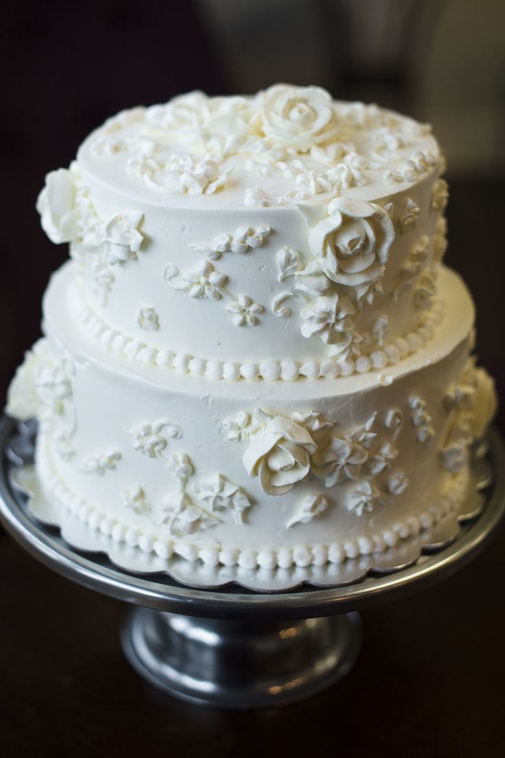 three tiered wedding cake with white flowers and pearls on the top, sitting on a silver platter