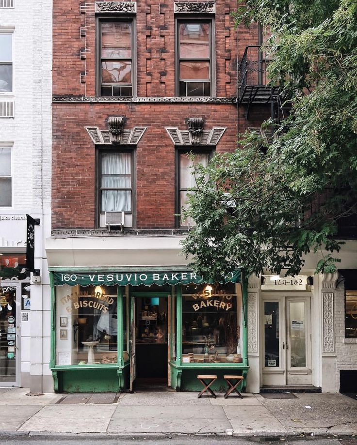 two people are walking down the sidewalk in front of an old brick building with green awnings