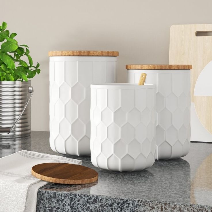 three white vases sitting on top of a counter next to a potted plant