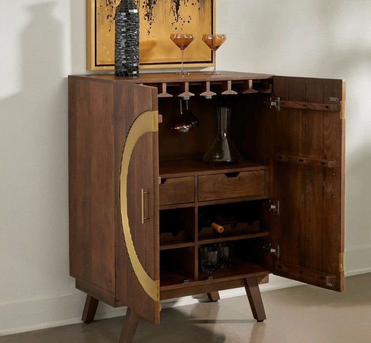 a wooden cabinet with wine glasses and bottles on the top, in front of a painting