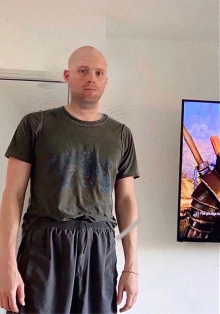 a bald man standing in front of a television with his hands on his hips and looking at the camera