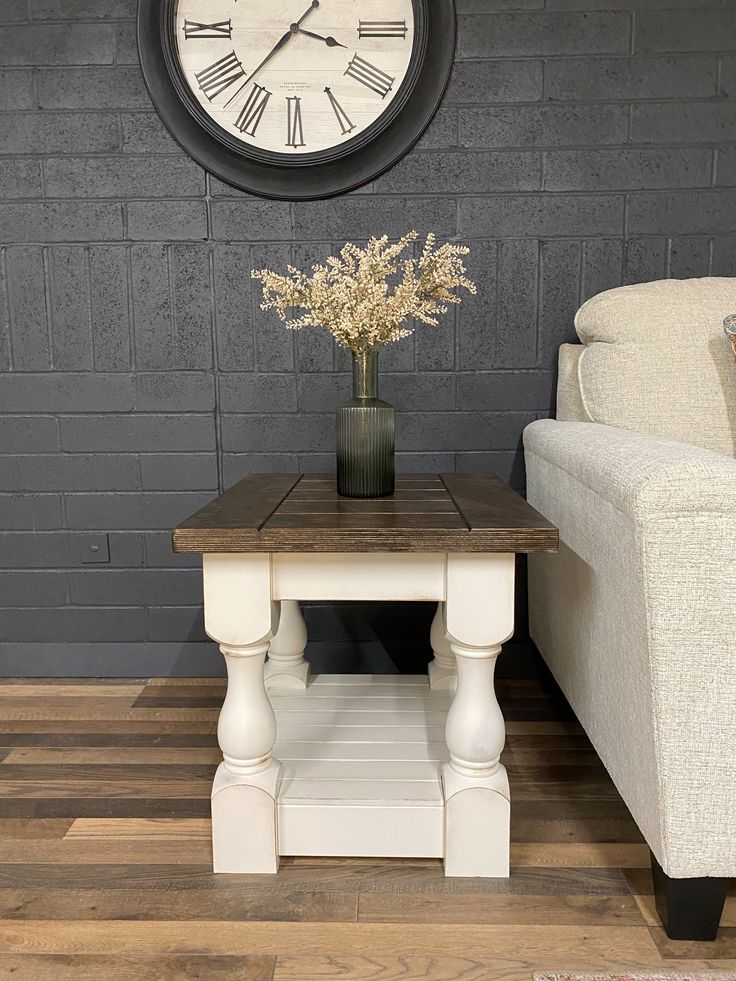 a white couch sitting next to a table with a vase on it and a clock above it