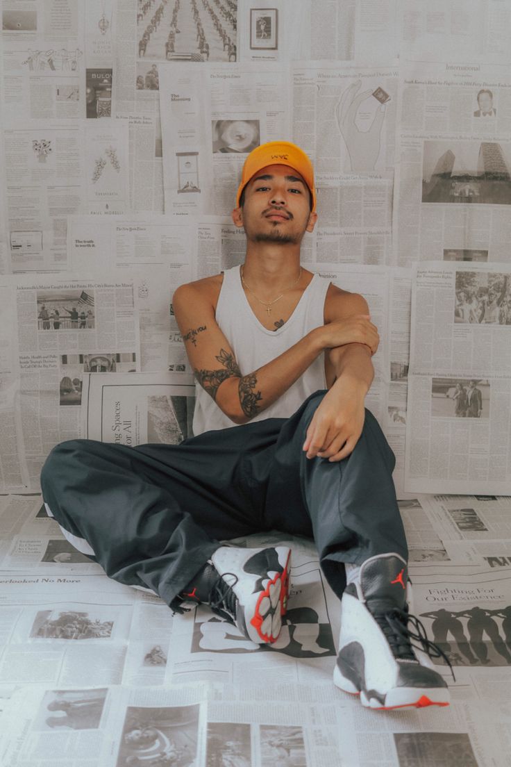 a man sitting on the floor with his legs crossed in front of him and wearing an orange hat