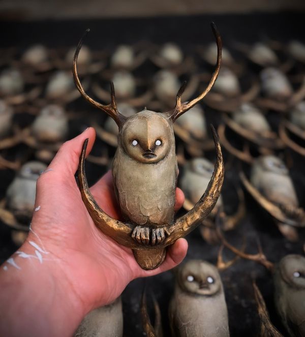 a hand holding a small toy owl with two smaller owls in the background