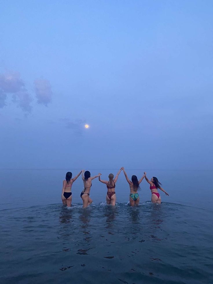 four girls in the water holding hands and jumping into the air at dusk or dawn