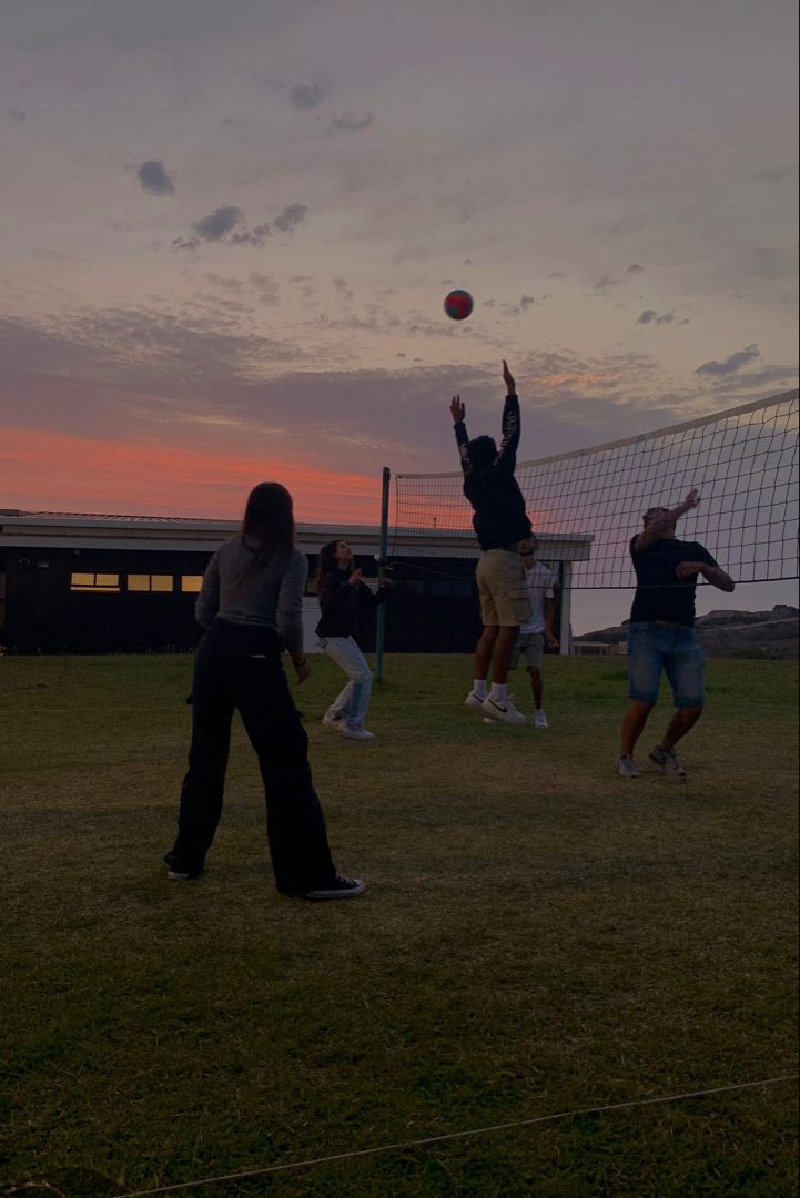 some people are playing with a ball in the field at sunset or sunrise, and one person is jumping up to catch it