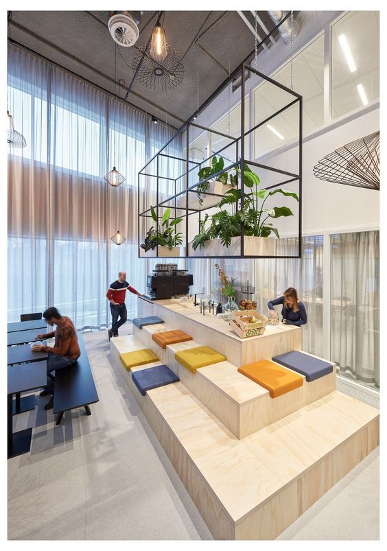 people are sitting at tables in an office with plants on the desks and shelves