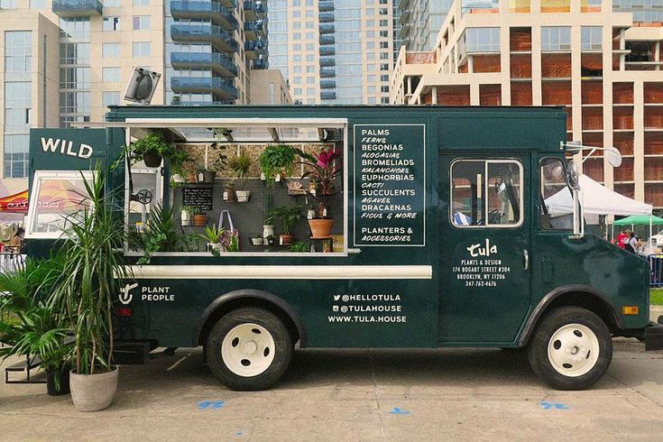 a green food truck parked in front of tall buildings with plants growing out of it