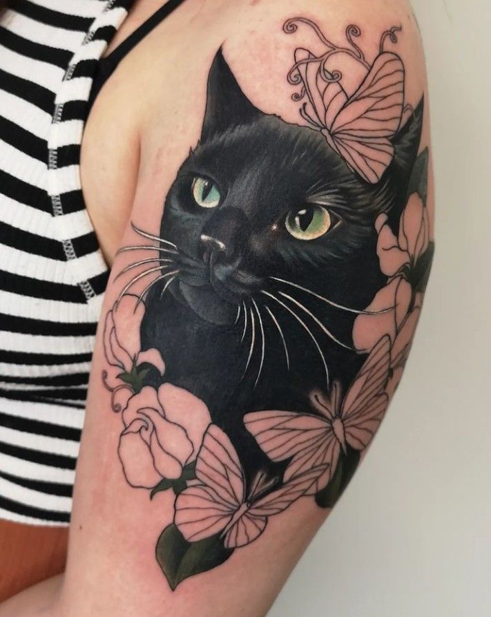 a black cat with green eyes surrounded by pink flowers and butterflies on the right arm