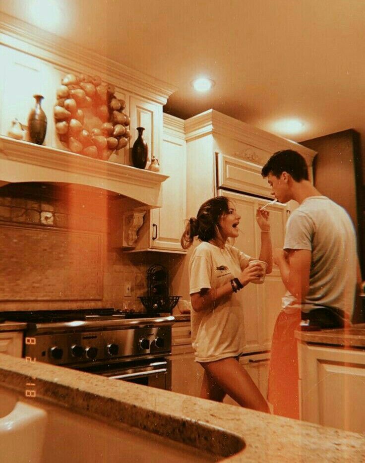 two people standing in a kitchen next to a sink and stove top with an oven