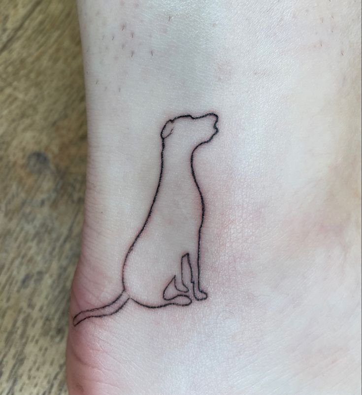 a small dog tattoo on the left side of the foot, which has a line drawing of a dog sitting down