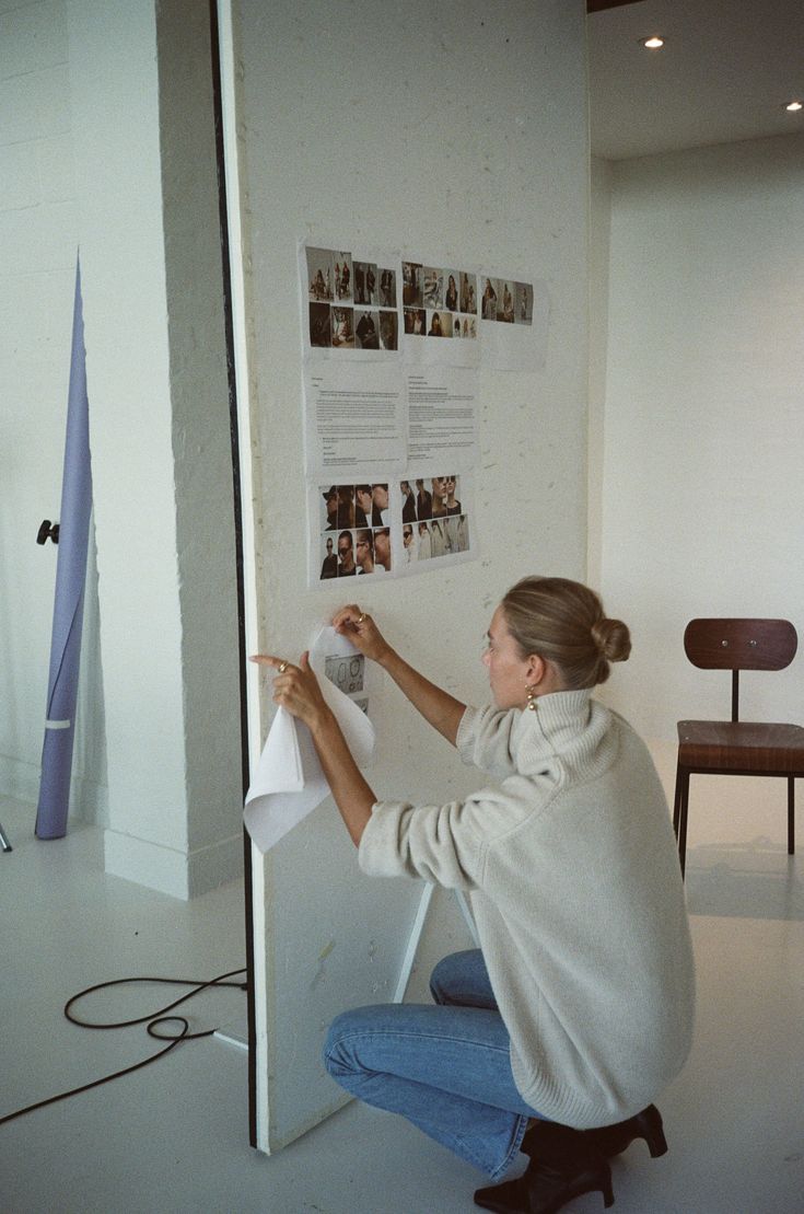 a woman sitting on the floor in front of a wall with pictures hanging on it