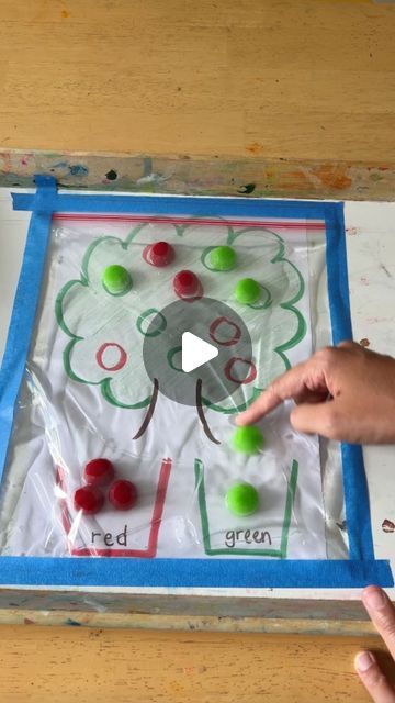 two hands pointing at an art project made with colored paper and gumballs on a wooden table