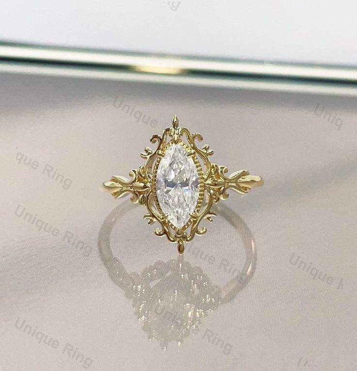 an ornately designed ring with a pear shaped diamond in the center on a white surface