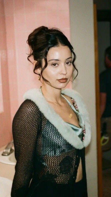 a woman standing in front of a bathroom mirror wearing a black dress and fur collar