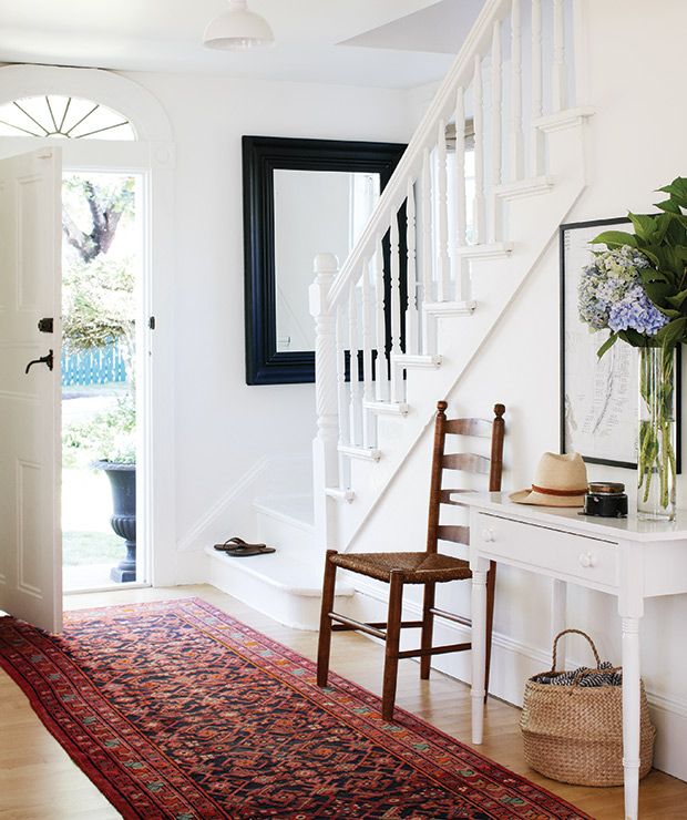 a room with a rug, chair and mirror on the wall next to a staircase