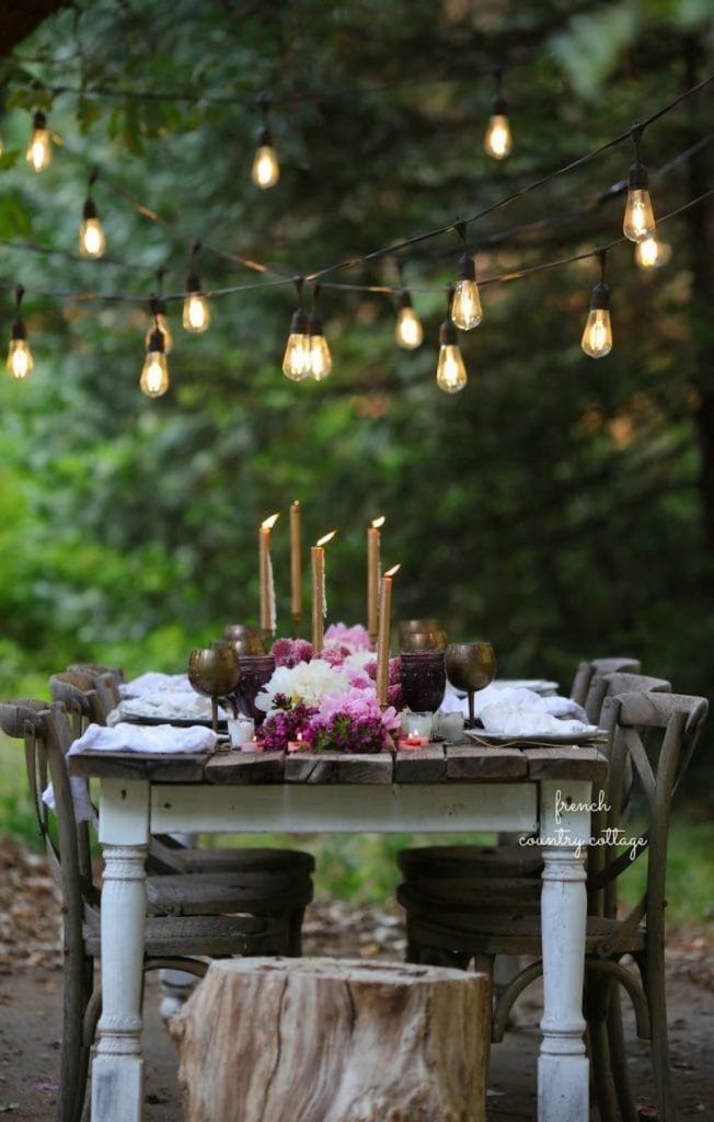 a table with candles and flowers on it in the middle of a forest surrounded by lights