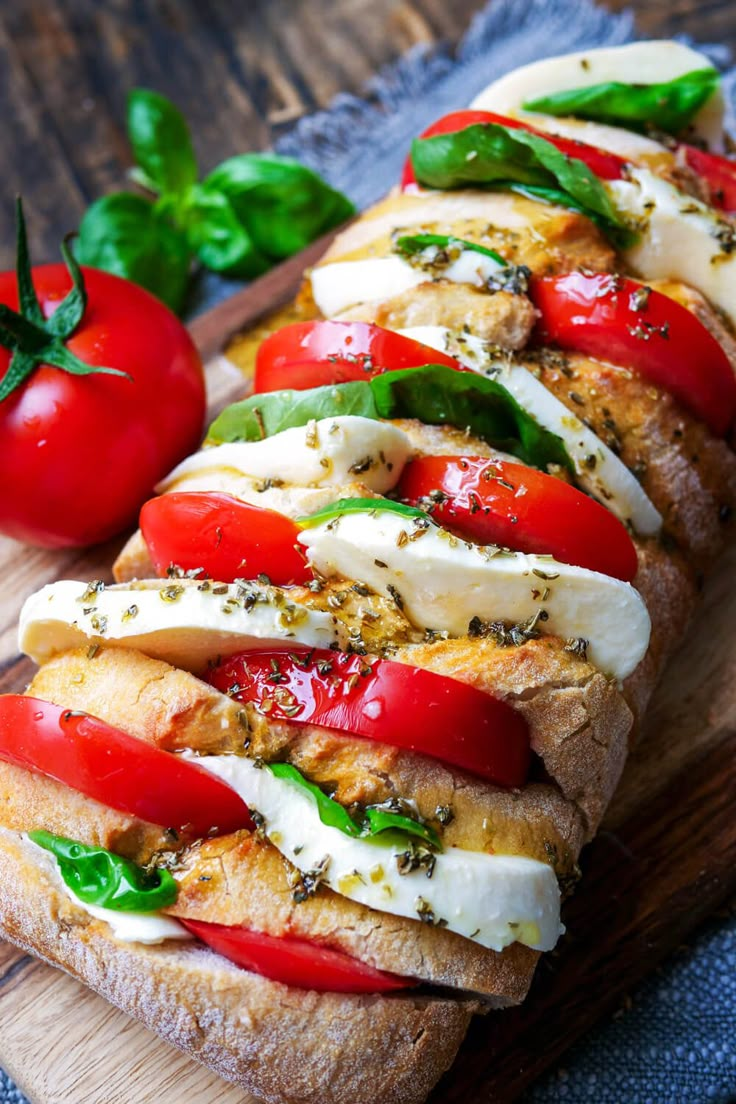 sliced bread with tomatoes, mozzarella and basil on wooden cutting board next to green leaves