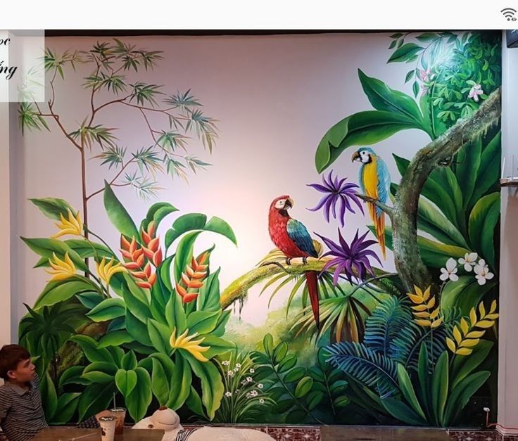 a man sitting in front of a mural with birds and tropical plants on the wall