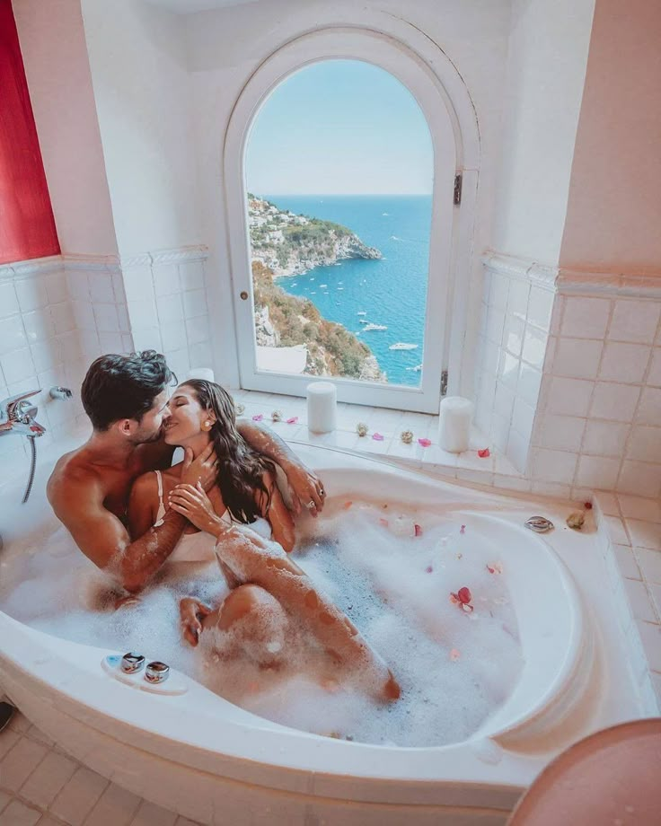 a man and woman are kissing in the jacuzzi bathtub with an ocean view