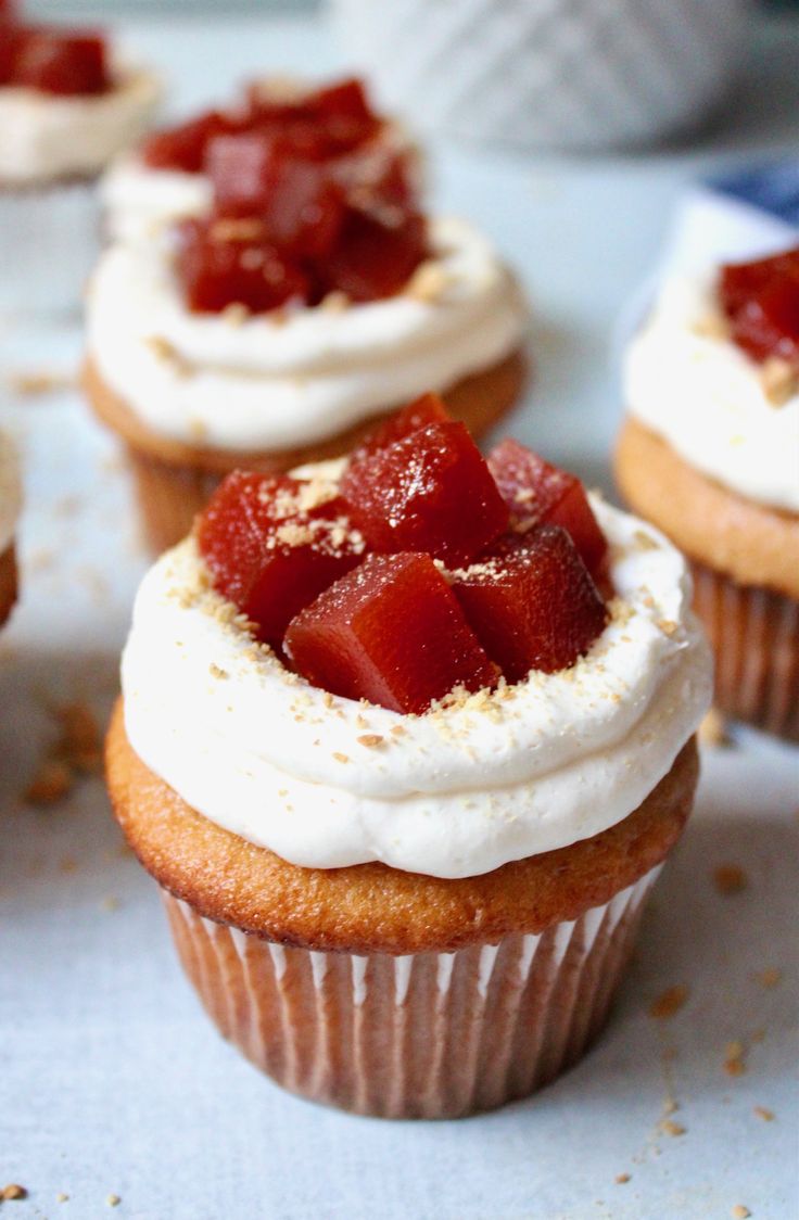 some cupcakes with white frosting and strawberries on top are sitting on a table