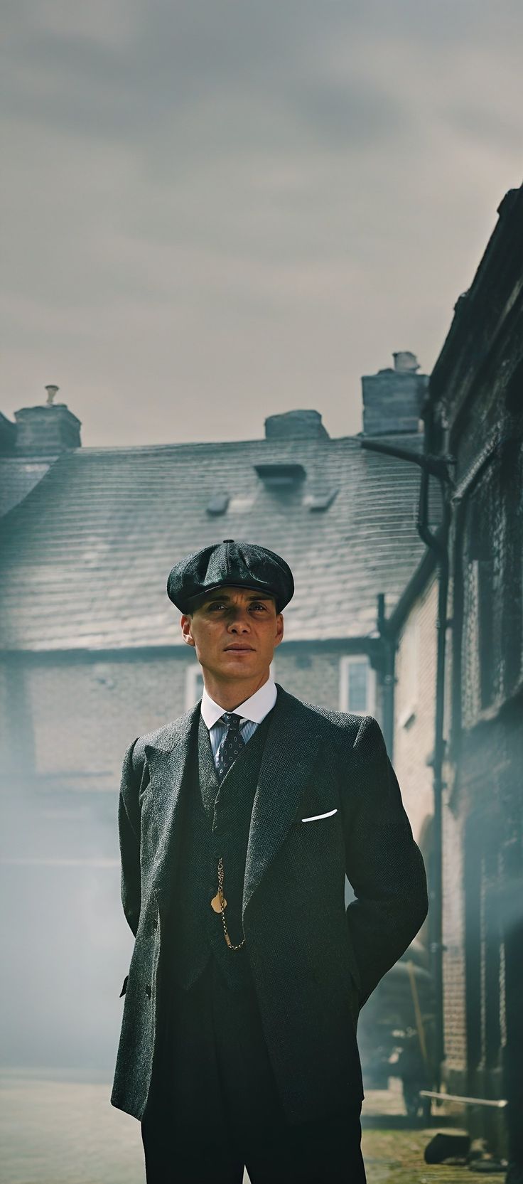 a man wearing a suit and hat standing in front of a building with his hands on his hips