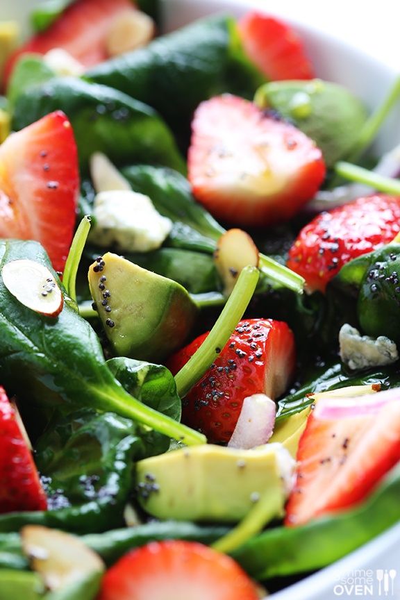 a salad with spinach, strawberries and avocado in a white bowl