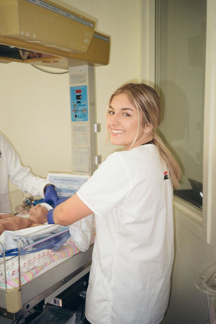 a woman in white shirt standing next to a baby on a hospital bed with medical equipment